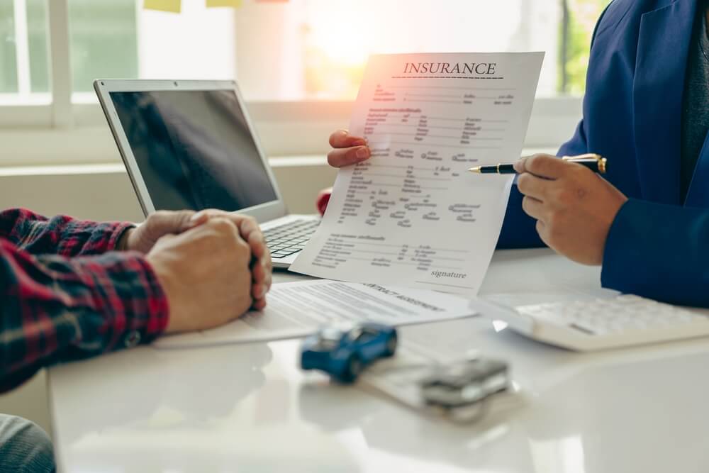 Insurance agent reviews a vehicle policy with a client at a desk, showing how to start a vehicle insurance franchise.