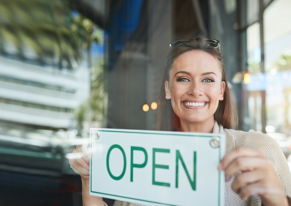 Business owner holding an open sign for a profitable motorcycle insurance franchise opportunity.