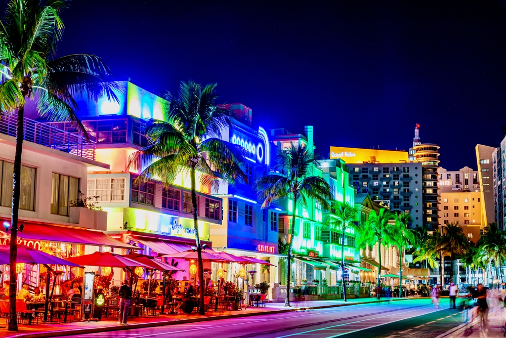 Neon-lit street in Miami with palm trees, restaurants, and colorful nightlife, creating a vibrant setting to open an insurance franchise in Miami.