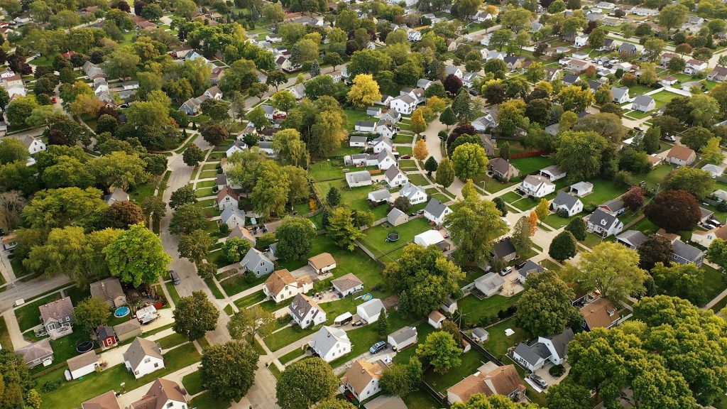 Aerial view of a suburban residential neighborhood with tree-lined streets and single-family homes surrounded by green yards.
