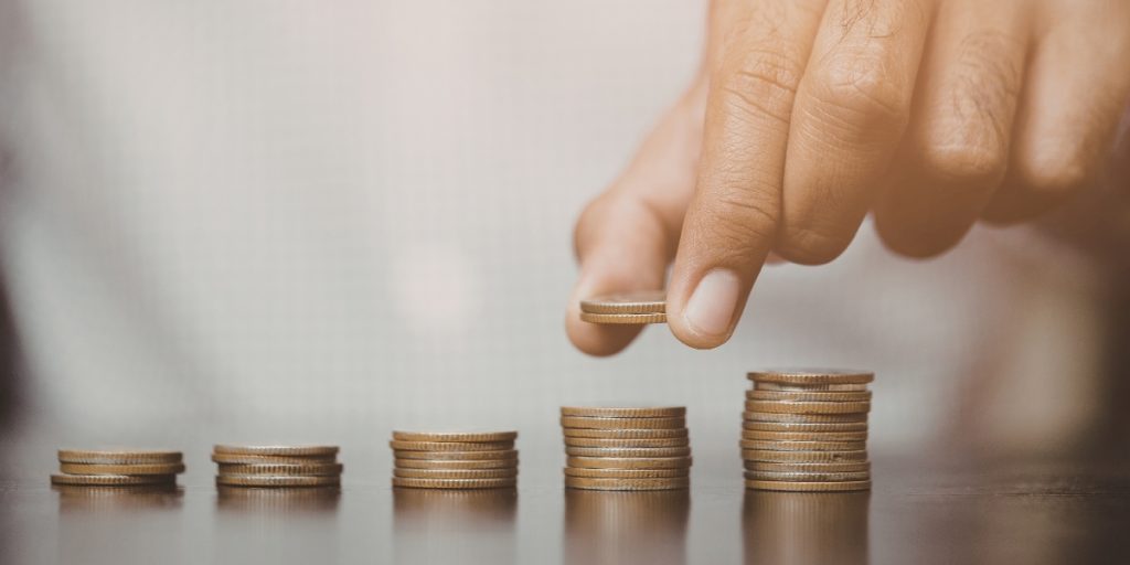 Hand placing coins into increasing stacks, symbolizing investment growth and long-term value in an insurance business