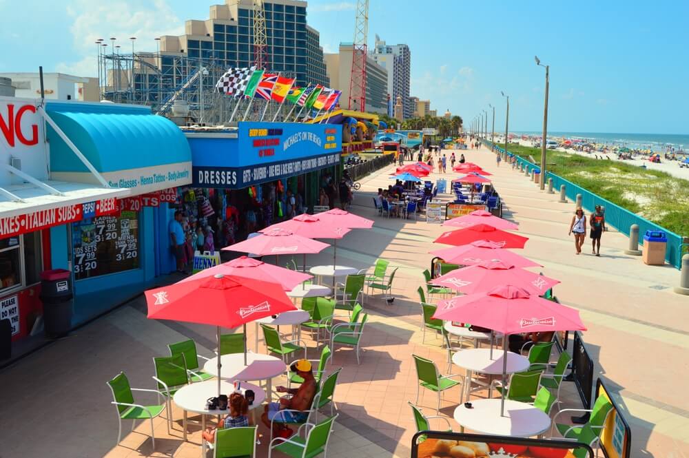 Paseo turístico junto a la playa con restaurantes, tiendas y visitantes, un entorno ideal para explorar ideas de negocios rentables en Florida.