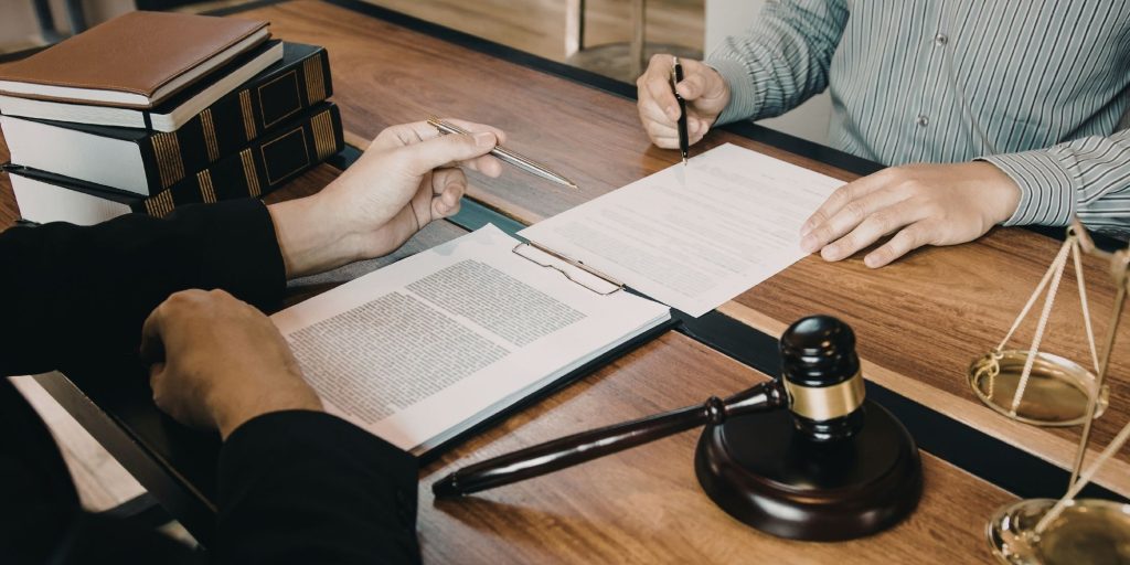 Dos personas revisando y firmando un contrato sobre un escritorio con documentos legales, libros y un mazo, simbolizando la formalización de un acuerdo de franquicia.