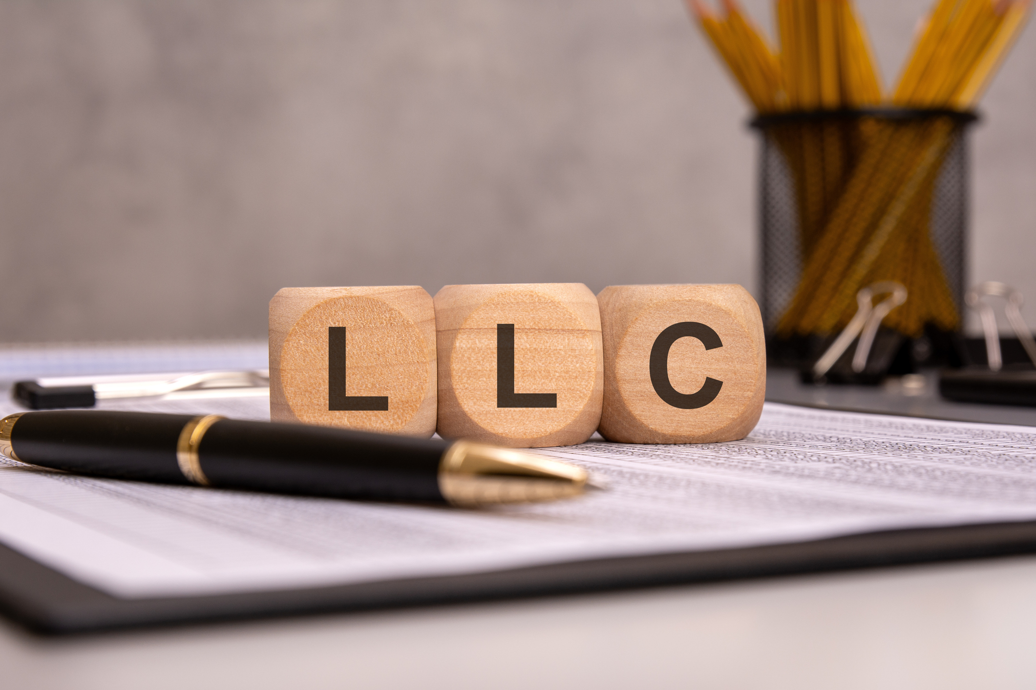 Cubos de madera con las letras “LLC” colocados sobre documentos legales, junto a una pluma, simbolizando la formación de una empresa de responsabilidad limitada en Estados Unidos.