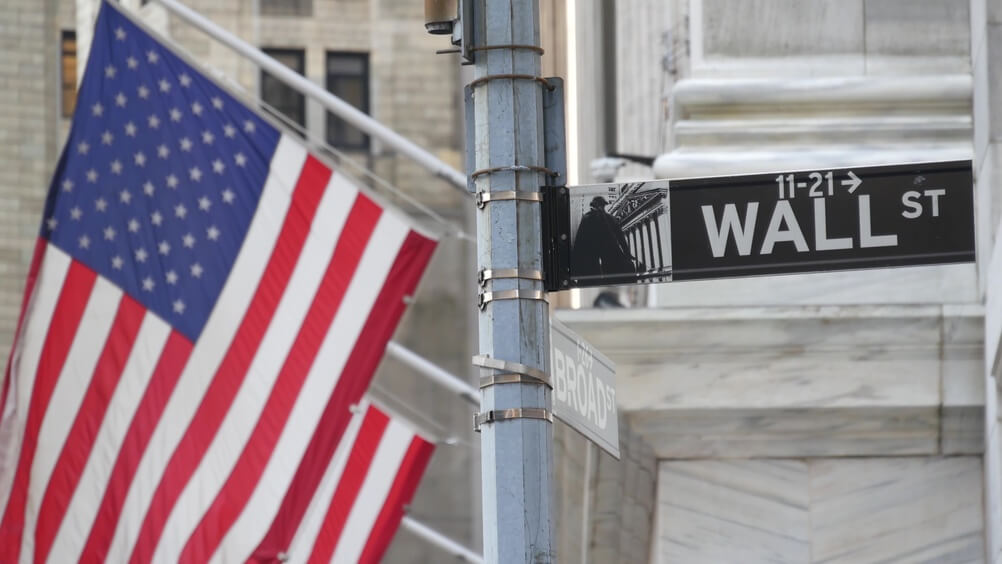 Letrero de Wall Street y bandera de Estados Unidos, representando el entorno económico y las oportunidades para desarrollar negocios rentables en New York.