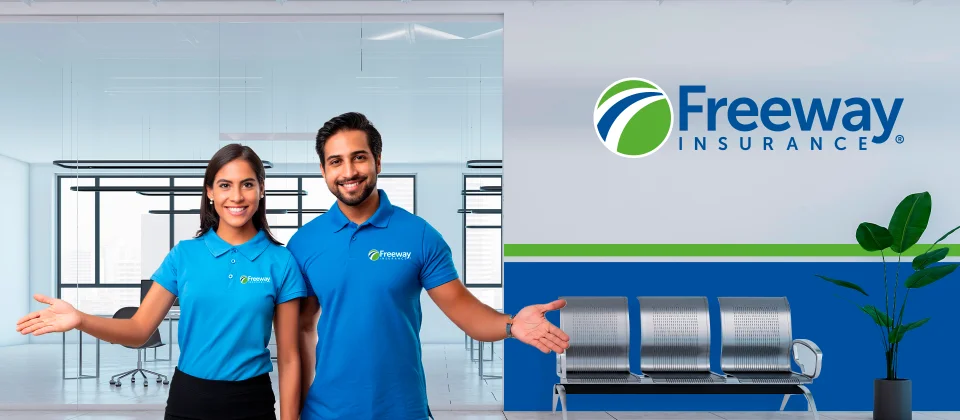 A smiling young Hispanic woman and man wearing Freeway Insurance shirts stand in a Freeway Insurance office with a welcoming hand held out.