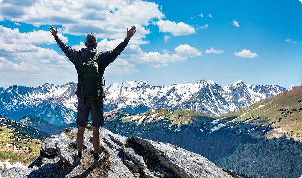 Hiker with arms up standing on the top of the mountain - Successful man enjoying triumph - Sport and success concept. Rocky Mountains National Park - open your own Freeway Insurance franchise in Colorado.