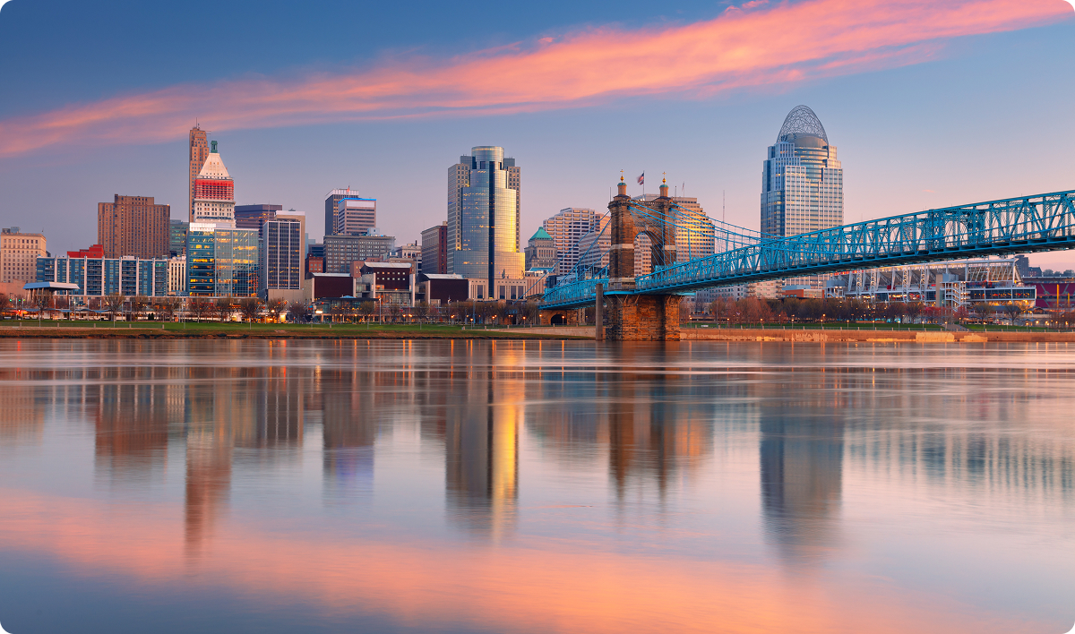 Cityscape image of Cincinnati, Ohio, USA downtown skyline with the John A. Roebling Suspension Bridge and reflection of the city in the Ohio River at spring sunrise.